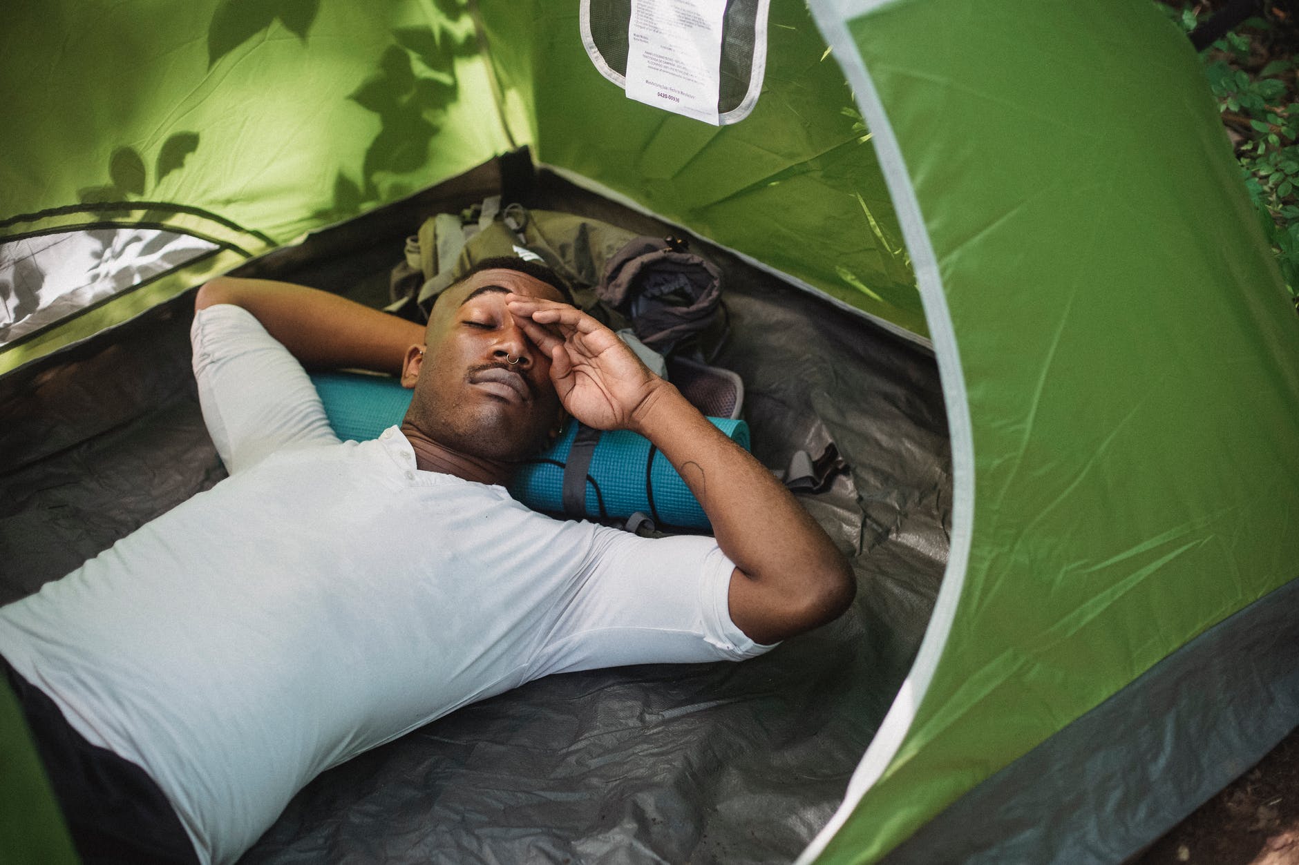 relaxed black man lying in tent while camping in nature